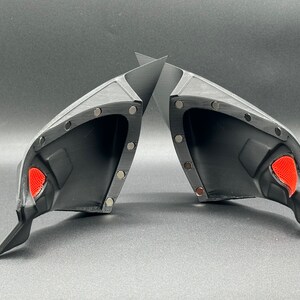 May include: Two black plastic car side view mirrors with red accents. The mirrors are designed to be attached to a vehicle.