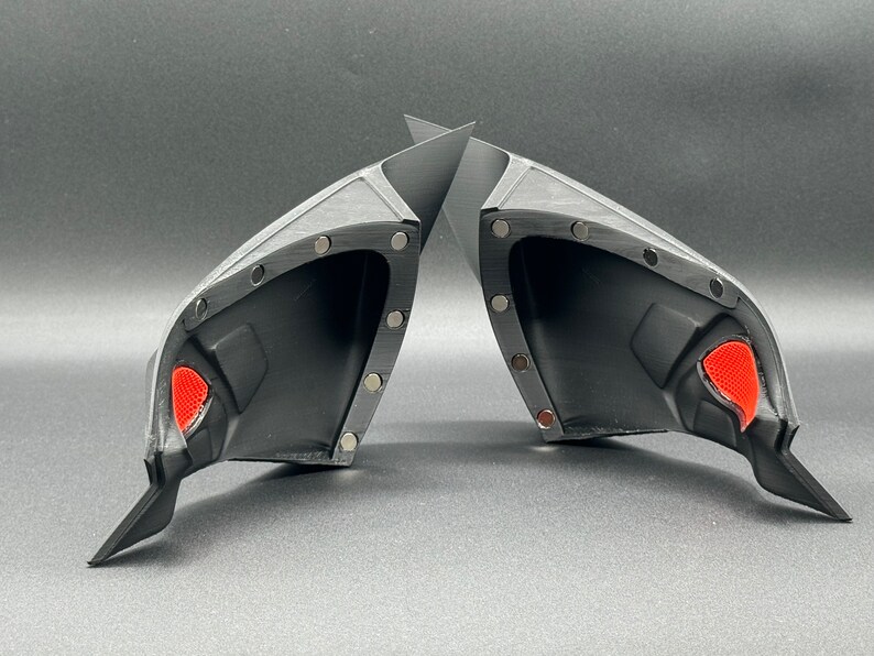 May include: Two black plastic car side view mirrors with red accents. The mirrors are designed to be attached to a vehicle.