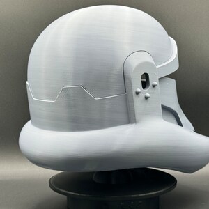May include: A white plastic helmet with a textured surface. The helmet has a rounded top and a curved bottom. The helmet has a small hole on the side and a series of small bumps on the back.