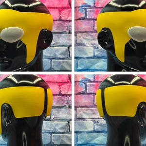 May include: A yellow headpiece featuring a smooth, solid-colored band that wraps around the forehead and sides, paired with white, oval-shaped mesh eye coverings. The accessory is displayed on a glossy black mannequin head from multiple angles.