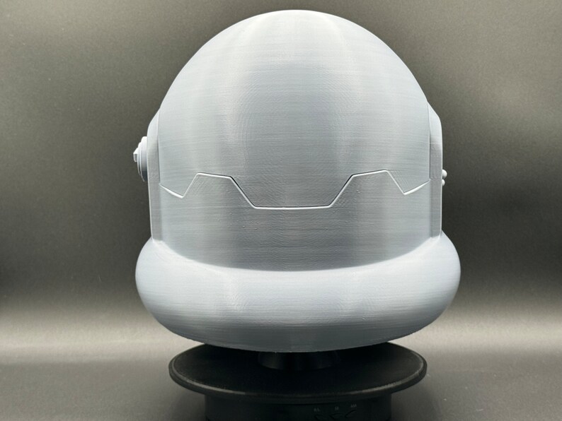 May include: A white 3D printed helmet with a rounded top and a textured surface. The helmet has a raised design around the bottom edge.