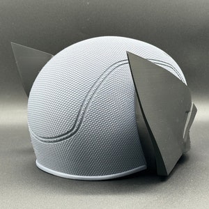May include: A gray and black 3D printed helmet with a textured surface and two pointed ears.