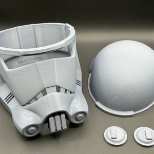 May include: A 3D printed white plastic helmet with a dome, faceplate, and two small round pieces. The helmet has the text "GALACTICARMORY" printed on the front.