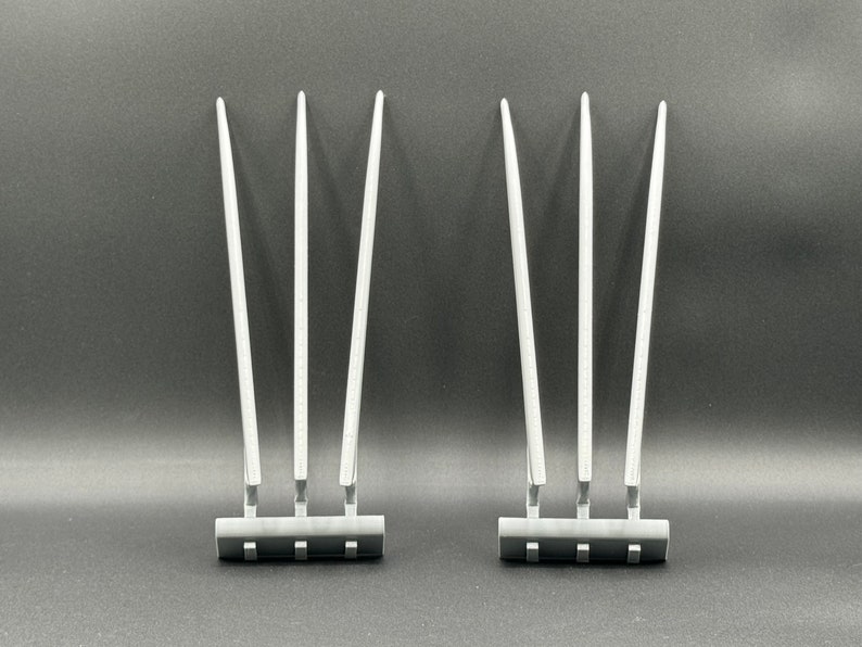 May include: Two sets of three silver-colored claws with a black base. The claws are long and thin, and they are arranged in a fan shape.
