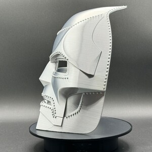 May include: A white 3D printed mask with a detailed design, resembling a character from a science fiction movie. The mask has a textured surface and a raised design around the eyes.