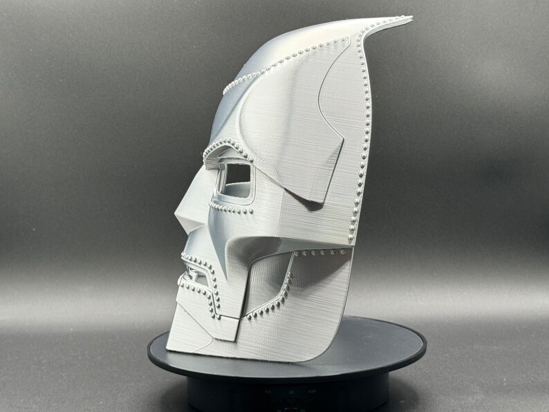 May include: A white 3D printed mask with a detailed design, resembling a character from a science fiction movie. The mask has a textured surface and a raised design around the eyes.
