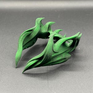 Puede incluir: Dos objetos verdes abstractos impresos en 3D con un dise&ntilde;o org&aacute;nico y fluido. Los objetos tienen una serie de elementos curvos y puntiagudos, y est&aacute;n colocados sobre una superficie gris. Los objetos parecen decorativos.