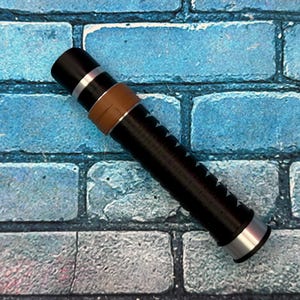 May include: A black and silver cylindrical object with a brown band and a series of white arrow-shaped markings. The object has a silver end cap and is set against a blue brick background.