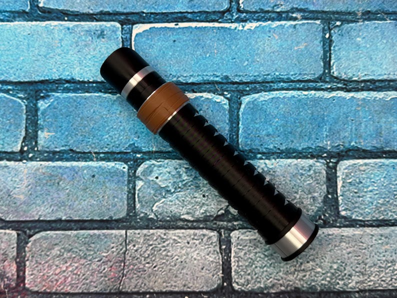 May include: A black and silver cylindrical object with a brown band and a series of white arrow-shaped markings. The object has a silver end cap and is set against a blue brick background.