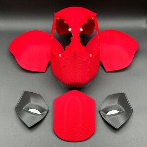 May include: A red and black 3D printed Deadpool mask with separate pieces for the eyes, mouth, and head. The mask is made of a textured material.