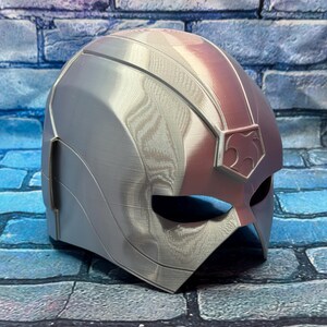 May include: A silver and red superhero helmet with a stylized design. The helmet features a smooth, metallic finish with a prominent crest on the forehead and eye openings. The color scheme is primarily silver with red accents.