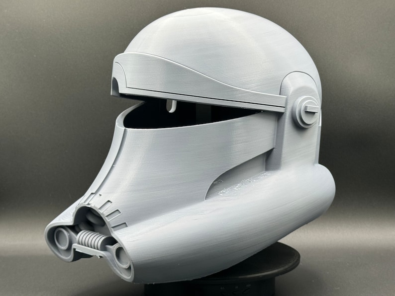 May include: A gray 3D printed helmet with a raised design. The helmet has a hinged visor and a detailed design on the front.