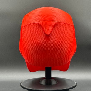 Puede incluir: Un casco rojo brillante con una superficie texturizada. El casco est&aacute; en un soporte negro.
