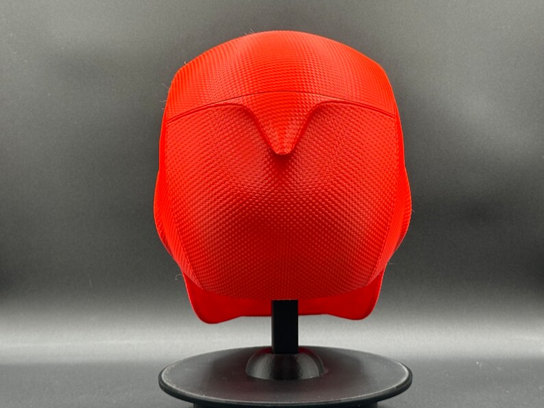 Puede incluir: Un casco rojo brillante con una superficie texturizada. El casco est&aacute; en un soporte negro.