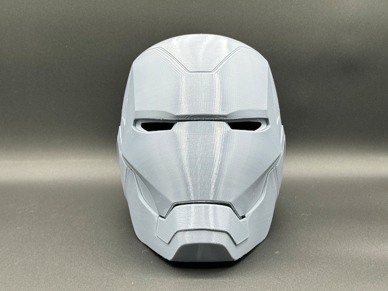 Puede incluir: Un casco de Iron Man gris impreso en 3D. El casco tiene un dise&ntilde;o detallado con una superficie texturizada.