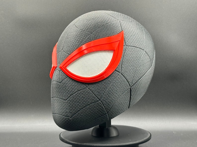 Puede incluir: Una m&aacute;scara de Spider-Man impresa en 3D de color negro y rojo con un patr&oacute;n de telara&ntilde;a y lentes de ojos rojos.