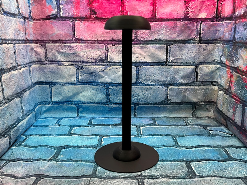 May include: A black hat stand with a round base and a tall, slender pole. The top of the stand has a curved, hat-shaped holder. The stand is made of metal and is designed to display hats.