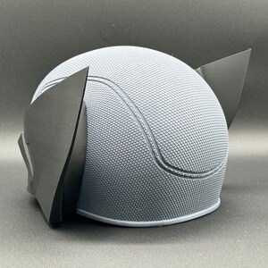 May include: A gray and black 3D printed helmet with a textured surface and two black ear pieces.