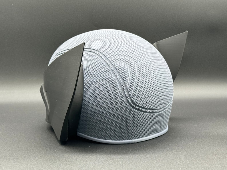 May include: A gray and black 3D printed helmet with a textured surface and two black ear pieces.