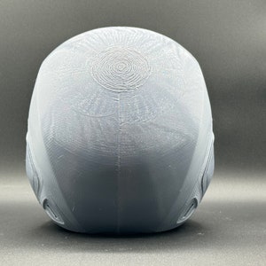 Puede incluir: Un casco gris impreso en 3D con una superficie texturizada y un patr&oacute;n circular en la parte superior.