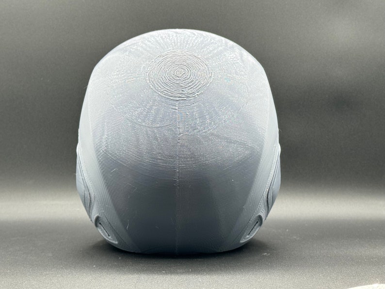 Puede incluir: Un casco gris impreso en 3D con una superficie texturizada y un patr&oacute;n circular en la parte superior.