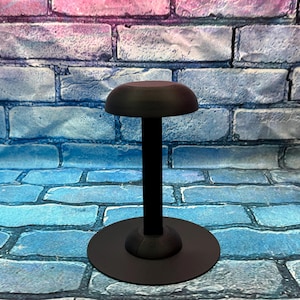 May include: A black hat stand with a round base and a domed top. The stand is made of a dark material and is designed to hold a hat. The stand is approximately 12 inches tall.