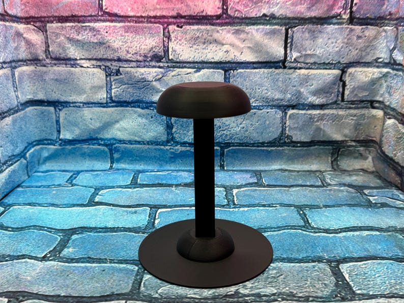 May include: A black hat stand with a round base and a domed top. The stand is made of a dark material and is designed to hold a hat. The stand is approximately 12 inches tall.