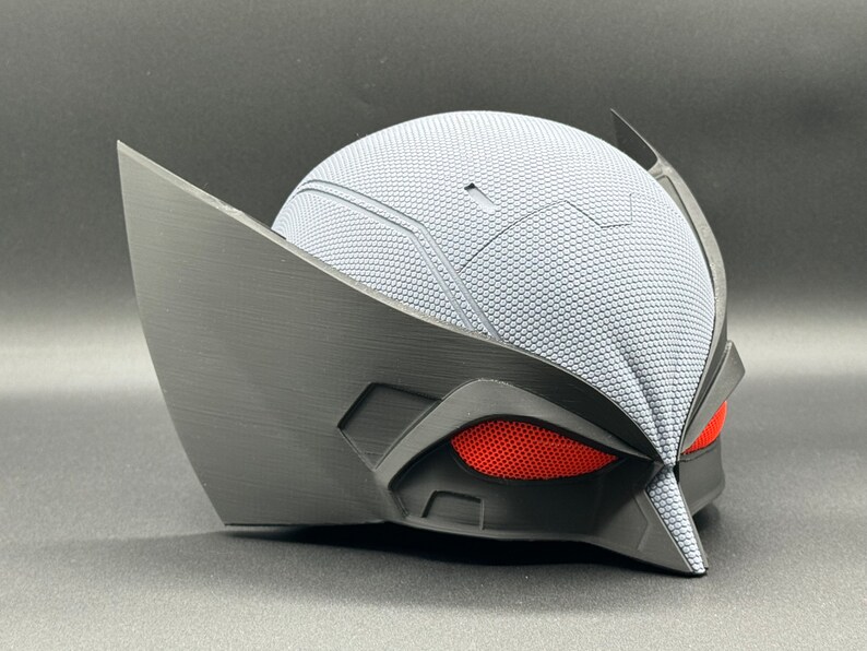 May include: A black and gray 3D printed helmet with red mesh eyes. The helmet has a textured surface and a pointed beak.