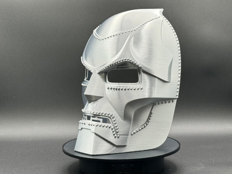 May include: A 3D printed silver mask of Doctor Doom, a fictional supervillain from Marvel Comics. The mask is detailed with rivets and has a textured surface.