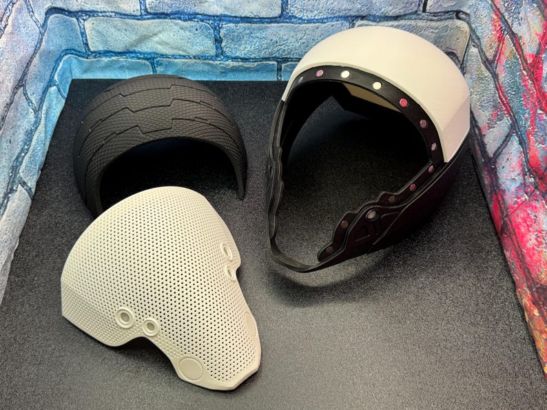 May include: Three-piece protective helmet set. Includes a white helmet with a black trim and a black helmet piece. The third piece is a perforated off-white face shield with circular openings.