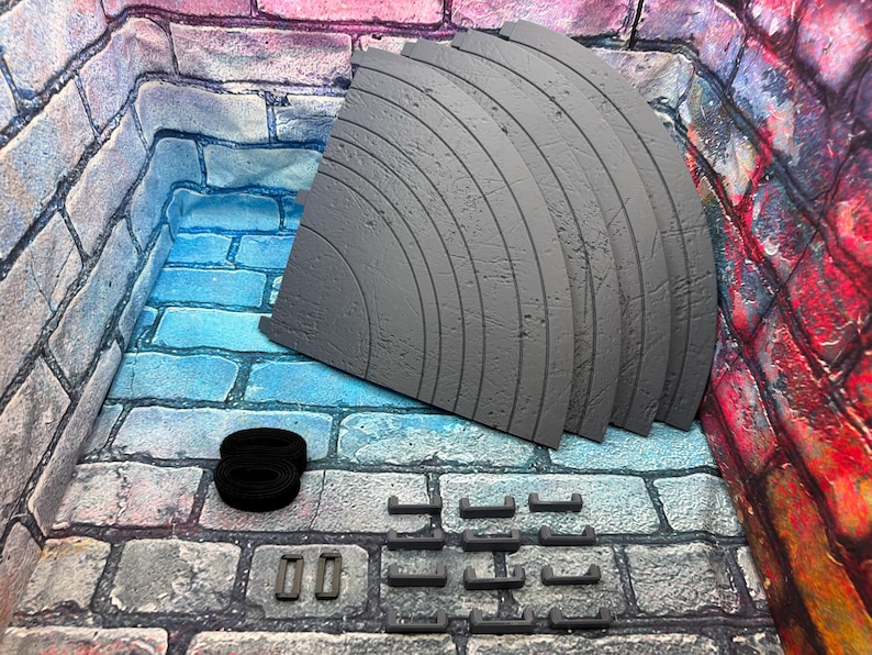 May include: A collection of gray, curved, segmented pieces, possibly for a diorama or model, with a textured surface. Also included are black straps and several small gray rectangular and curved pieces. The items are arranged on a brick-patterned surface.
