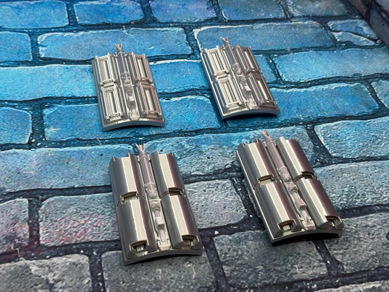 以下が含まれることがあります： 青とグレーのレンガ模様の表面に配置された、詳細な建築デザインの4つの銀色の長方形のオブジェクト。 各ピースは、中央の垂直要素と湾曲したベースを備えています。