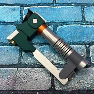 May include: A multi-colored tool with a green handle, silver body, and orange accent. The tool has a silver blade and is set against a blue brick background. The tool appears to be a specialized instrument.