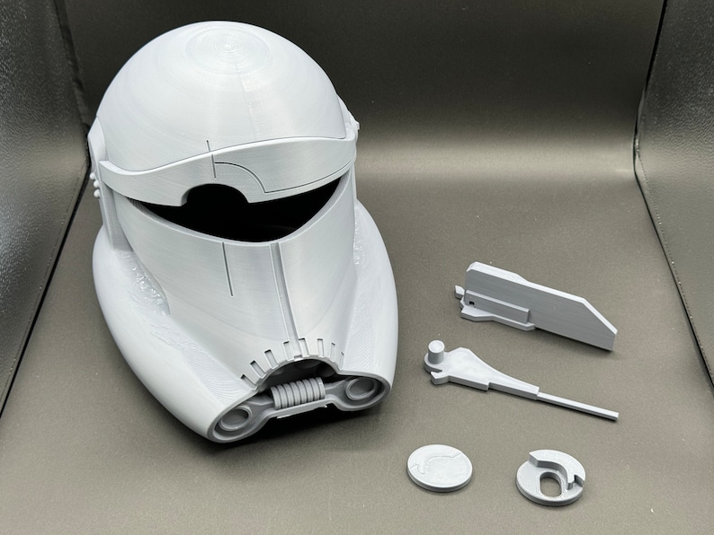 May include: A white plastic helmet with a visor and a spring-loaded jaw. The helmet is disassembled into several pieces, including the helmet itself, the visor, the jaw, and two small circular pieces.