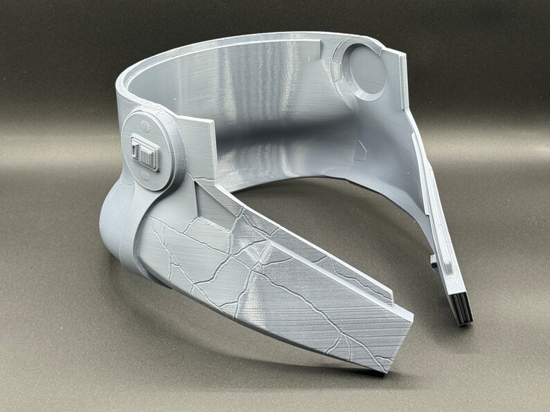 May include: A gray plastic helmet with a textured surface and a small, round button on the side. The helmet is in two pieces, with the front piece separated from the back piece.