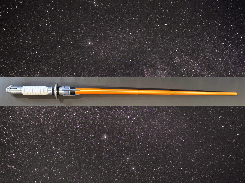 May include: An orange lightsaber with a silver and white hilt. The lightsaber is displayed against a starry background. The hilt features a white grip and silver accents. The blade is a bright orange color.