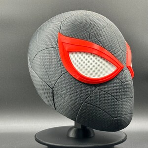 Puede incluir: M&aacute;scara de Spider-Man impresa en 3D de color negro y rojo con un dise&ntilde;o de telara&ntilde;a y lentes de ojos rojos.