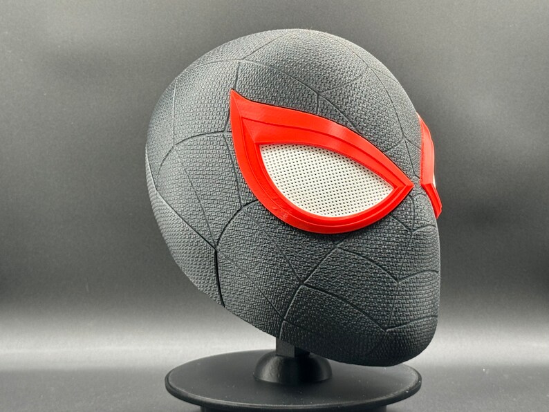 Puede incluir: M&aacute;scara de Spider-Man impresa en 3D de color negro y rojo con un dise&ntilde;o de telara&ntilde;a y lentes de ojos rojos.