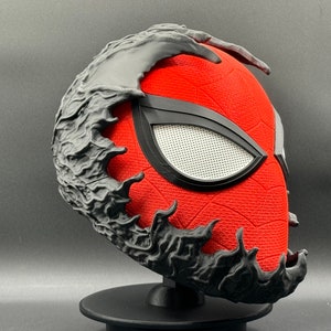 Puede incluir: Una m&aacute;scara roja y negra impresa en 3D con una superficie texturizada. La m&aacute;scara tiene un dise&ntilde;o negro de ara&ntilde;a en la parte superior y una pieza de ojo negra con una malla blanca.