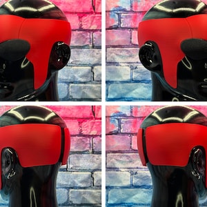 May include: A bright red, smooth, wrap-around headpiece worn on a glossy black mannequin head. The headpiece features a wide, solid band that covers the forehead and extends down the sides, with dark, oval-shaped eye coverings integrated into the design.