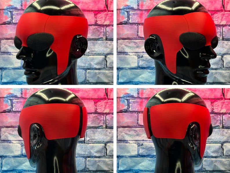 May include: A bright red, smooth, wrap-around headpiece worn on a glossy black mannequin head. The headpiece features a wide, solid band that covers the forehead and extends down the sides, with dark, oval-shaped eye coverings integrated into the design.