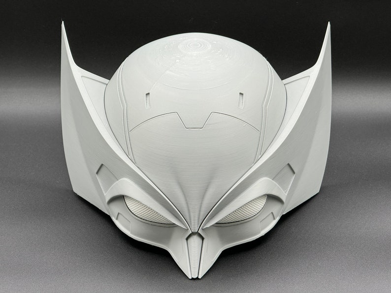 Puede incluir: Una m&aacute;scara blanca impresa en 3D con un dise&ntilde;o detallado. La m&aacute;scara tiene una barbilla puntiaguda y grandes agujeros para los ojos angulares.
