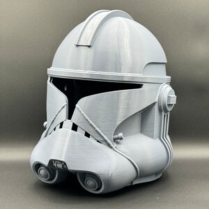 Puede incluir: Un casco gris de pl&aacute;stico impreso en 3D con un dise&ntilde;o detallado. El casco tiene una visera y una superficie texturizada.
