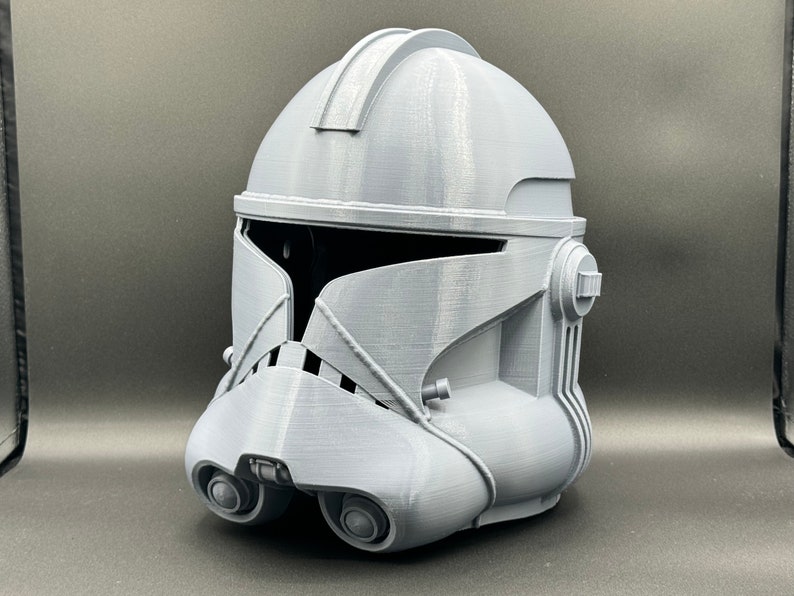Puede incluir: Un casco gris de pl&aacute;stico impreso en 3D con un dise&ntilde;o detallado. El casco tiene una visera y una superficie texturizada.