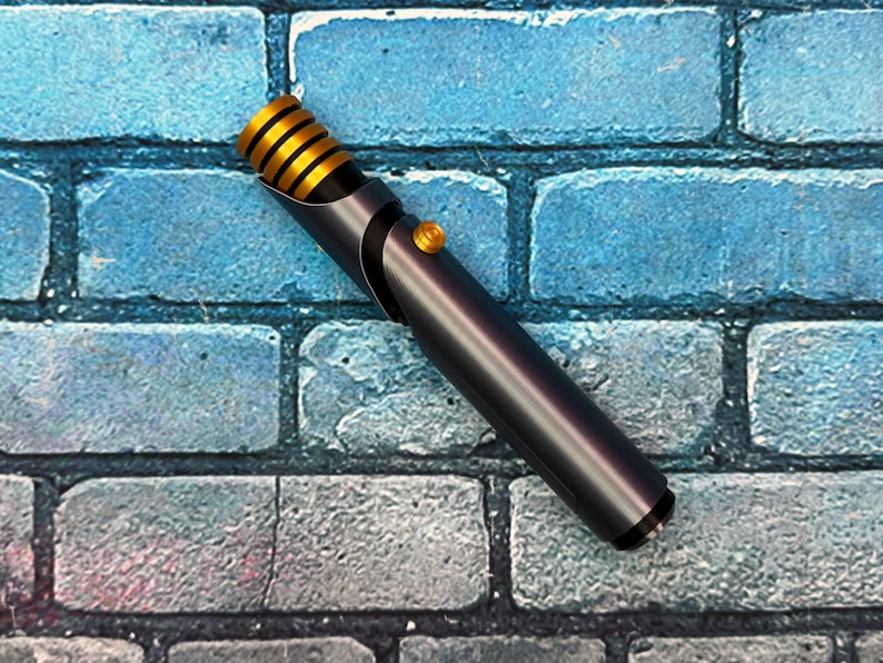 May include: A metallic gray lightsaber with gold accents and a gold button. The hilt has a black grip and a gold-colored emitter. The lightsaber is set against a blue brick wall.
