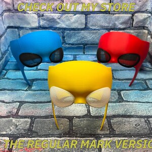May include: Three superhero-style masks in blue, red, and yellow, each featuring mesh eye coverings. The text CHECK OUT MY STORE FOR THE REGULAR MARK VERSIONS is visible at the top and bottom of the image against a brick wall background.