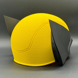 May include: Yellow and black plastic costume mask with a textured surface. The mask is shaped like a head with two pointed ears.