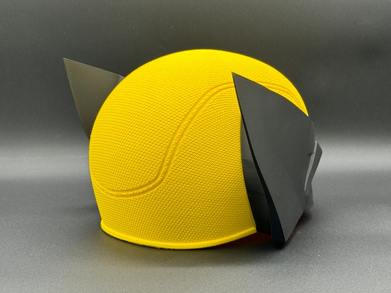 May include: Yellow and black plastic costume mask with a textured surface. The mask is shaped like a head with two pointed ears.