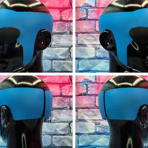 May include: A bright blue textured headband worn on a glossy black mannequin head. The headband features a wide, contoured design that wraps around the forehead and extends down to cover the ears, showcasing a consistent dimpled surface pattern.