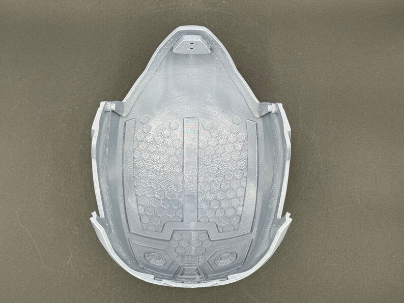 Puede incluir: Un casco gris impreso en 3D con un patr&oacute;n de panal en el interior. El casco tiene una secci&oacute;n elevada en la parte superior con dos peque&ntilde;os agujeros.